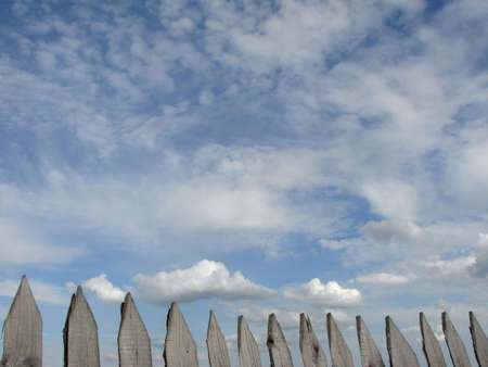 fragment of the old wooden fence at the background of blue sky with clouds                               の写真素材