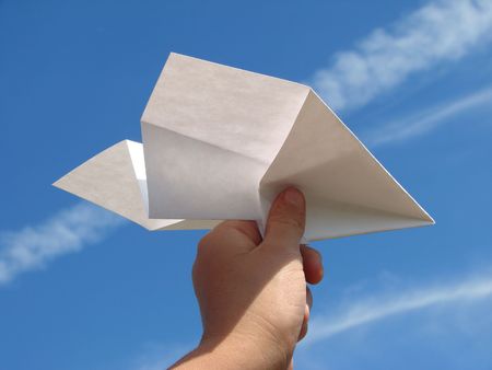 child hand with paper plane against blue sky                               の写真素材