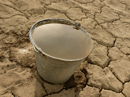 bucket full of water on dry soil backgroundの写真素材