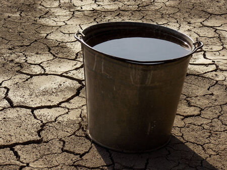 bucket full of water on dry soil backgroundの写真素材