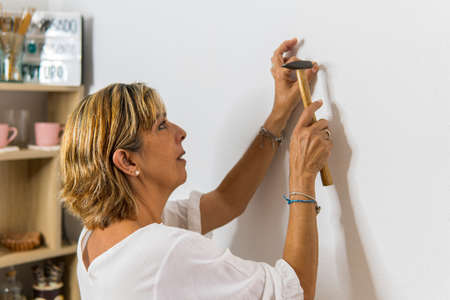 Adult woman with a hammer to hammer a nail into the wall in order to hang a picture.の写真素材