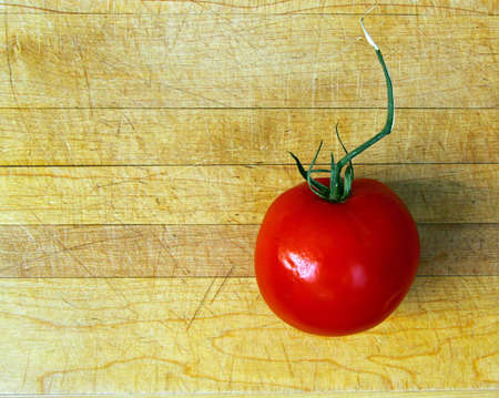 Red tomato with twisted stem on rustic cutting board.の写真素材
