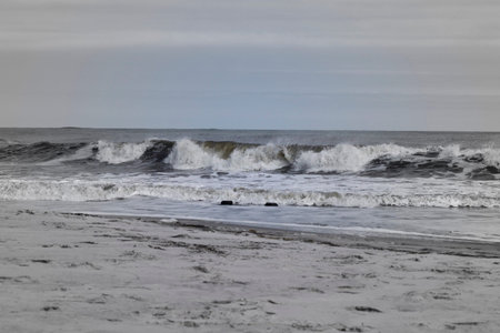 Pastel colored photo of ocean waves breaking, sand in the foreground.