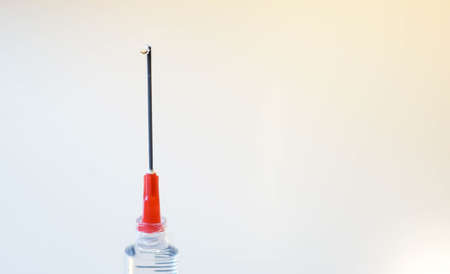 A syringe needle is help vertically and a drip of fluid exits and runs down the needle against a white backgroundの写真素材