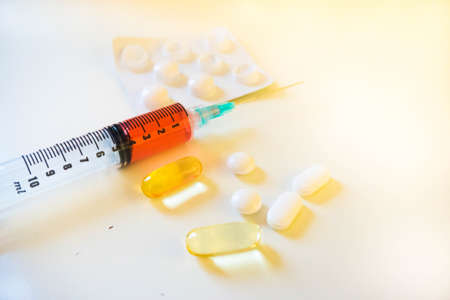 A syinge containing 4ml of red fluid sits next white and yellow pills and a blister pack from close upの写真素材