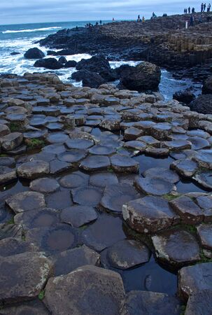 View of the Rocks of Giants Causeway with sea sprayed rocks and Ocean behind with touristsの写真素材