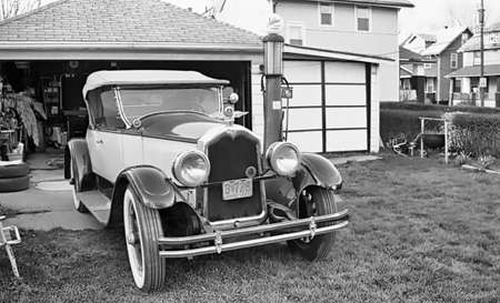 This is a photograph of a classic car in front of it's storage garage and an old gasoline pump.の写真素材