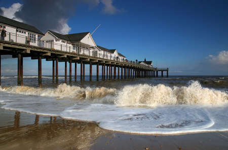 Southwold Pier in Suffolk, UK. White pier buildings against a blue sky with waves breaking on a sandy beach in the forground.の写真素材