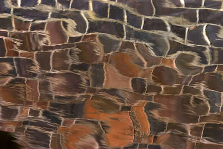 Colorful brick patterns reflected in calm gentle water. Ripples distorting the soft brown & blue colors.の写真素材