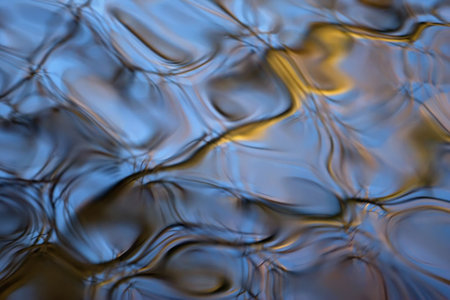 Abstract pattern of a trees sunlight golden branches reflecting in blue rippling water.