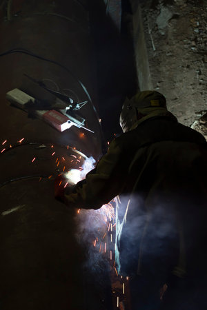 male worker welds steel pipe of household heating at night