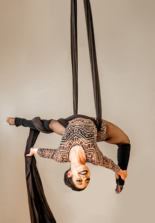 Young woman doing acrobatic tricks with aerial silks on gray backgroundの写真素材