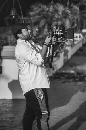Young handsome man with beard and mustache in black hat and white shirt holding professional camera...