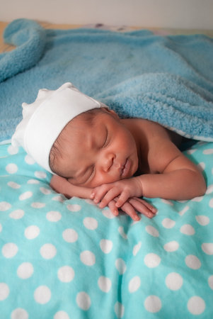 Newborn baby boy sleeping on a blue blanket with a white hatの写真素材