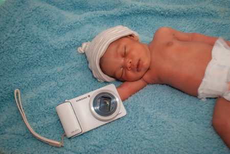 Newborn baby boy sleeping with a camera on a blue blanket.の写真素材