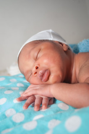 Newborn baby boy sleeping on a blue blanket in a white capの写真素材