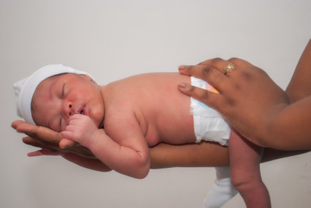 Newborn baby in a white bodysuit sleeping on his mother's handsの写真素材