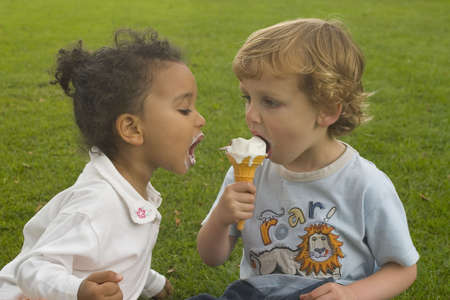 Two young children sharing an ice cream cone.の写真素材