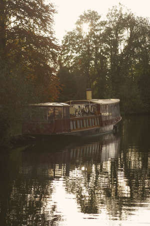 The sun sets behind a river cruising boat on the River Thames, Englandの写真素材