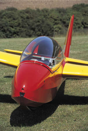 A red and yellow glider resting on a grass airfieldの写真素材