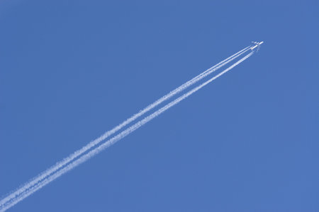 A jumbo jet flies through a perfect blue sky leaving vapour trails in it's wake