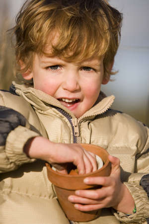 A young boy with a stack of flower pots in a sunny gardenの写真素材