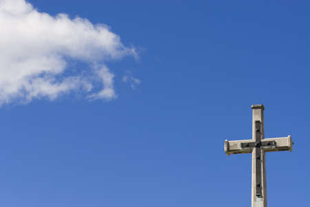 A crucifix shot against a blue sky with a white cloudの写真素材