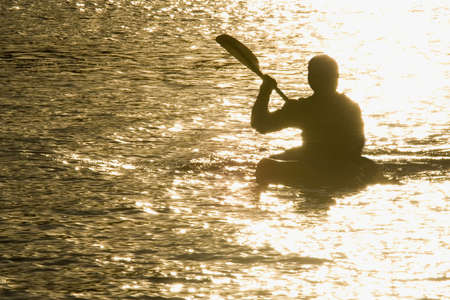 A kayaker paddles across a lake illuminated by the setting sun.の写真素材