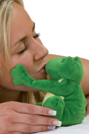 A beautiful young blond woman laying on white bed sheets kisses a very lucky frog who gently caresses her cheek!の写真素材