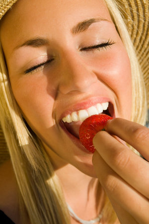 Close up shot of a stunningly beautiful young blond woman ecstatically eating a strawberry lit by golden summer sunshine.の写真素材