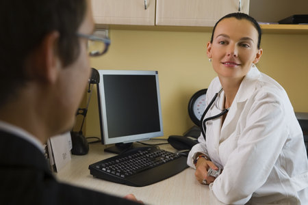 A male patient in consultation with a female doctor, behind her is a blood pressure monitor.