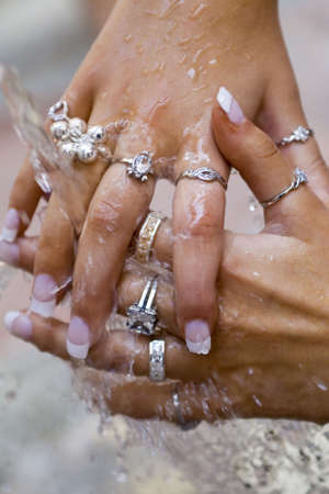 Beautifully manicured women's hands covered in rings being washed outside under free flowing waterの写真素材