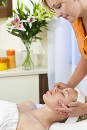 A young woman relaxing at a health spa while having a facial treatmentの写真素材