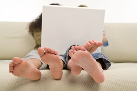 Two young children surfing the wold wide web on a laptop while sitting on a settee
