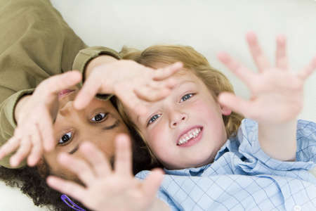 A beautiful young mixed race girl and a cute blond boy laying down and reaching up to the cameraの写真素材