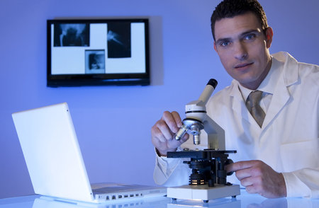 A male medical or scientific researcher using his microscope and laptop, behind hima are some x-rays on a light boxの写真素材