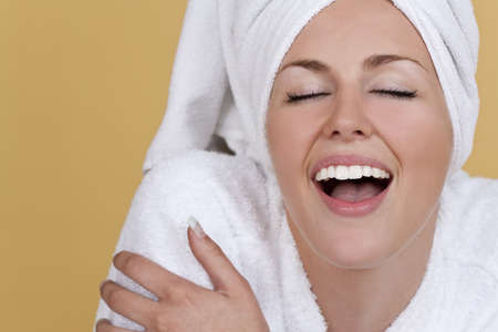 A beautiful young woman in a toweling robe and her hair in a towel looking ecstatically happyの写真素材
