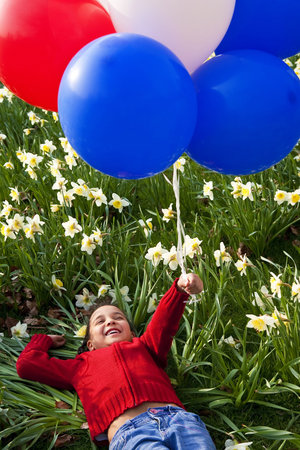 A beautiful young mixed race girl playing with balloons in a field of daffodilsの写真素材