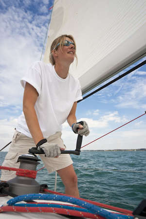 Shot of beautiful young woman on the deck of a boat operating a winch to hoist a sailの写真素材
