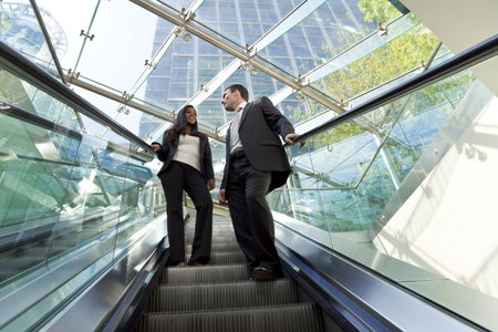 A young male and female executive ride an escalator together in a modern hi-tech city settingの写真素材