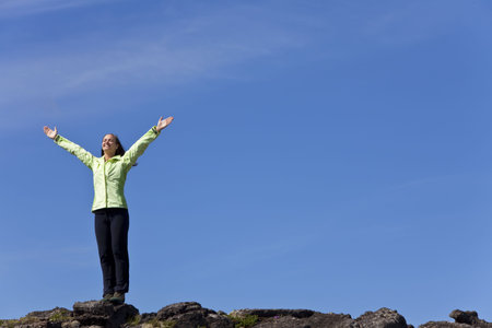 A beautiful young woman stands on the horizon arms raised celebrating reaching the top of a...