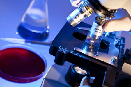 A medical or scientific researcher using a microscope in a laboratory environment with conical flask, pipette and petri dishの写真素材