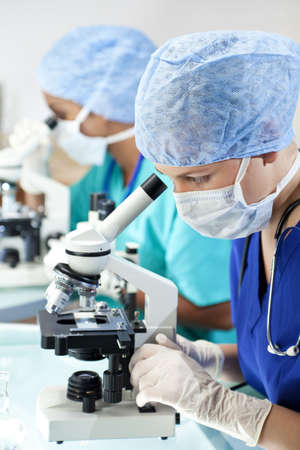 Two female medical or scientific researchers or doctors, one asian one european, using microscopes in a laboratory.の写真素材