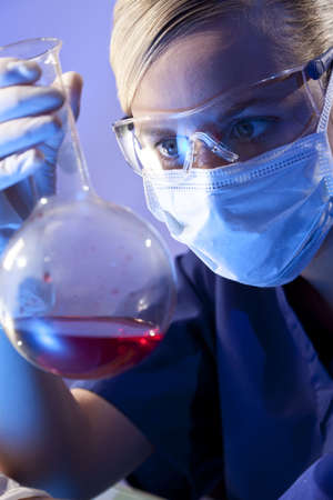 A female medical or scientific researcher or doctor looking at a flask of red liquid in a laboratory.の写真素材