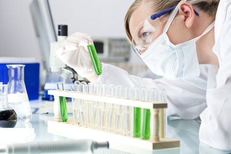 A female medical or scientific researcher or doctor looking at a test tube of green solution in a...