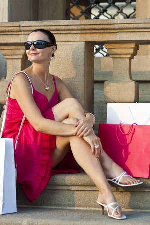 A classically beautiful Mediterranean woman sitting and thinking surrounded by full shopping bagsの写真素材