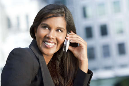 A beautiful young Asian businesswoman with a wonderful smile chatting on her cell phone with an out of modern city behind her.の写真素材