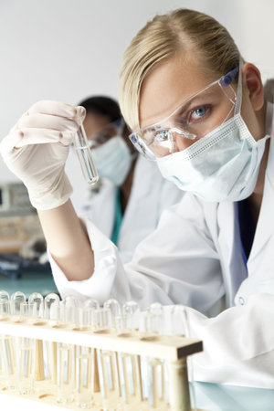 A blond medical or scientific researcher or doctor using looking at a clear solution in a laboratory...