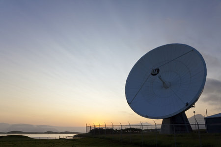 A radio telescope at sunset with the sun going down behind it producing amazing cloud strata...