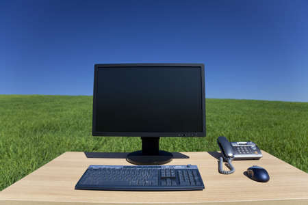 Business concept shot showing a computer on a desk in a green field with a blue sky. Shot on location not in a studio.の写真素材